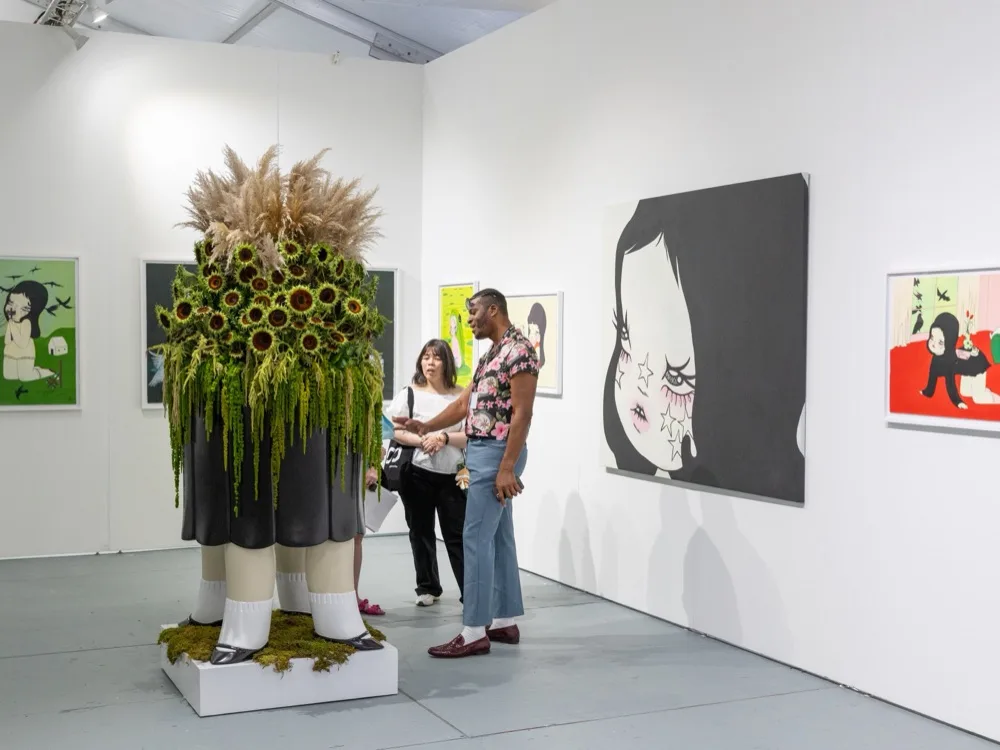 Visitors in a gallery booth beside a tall sculpture