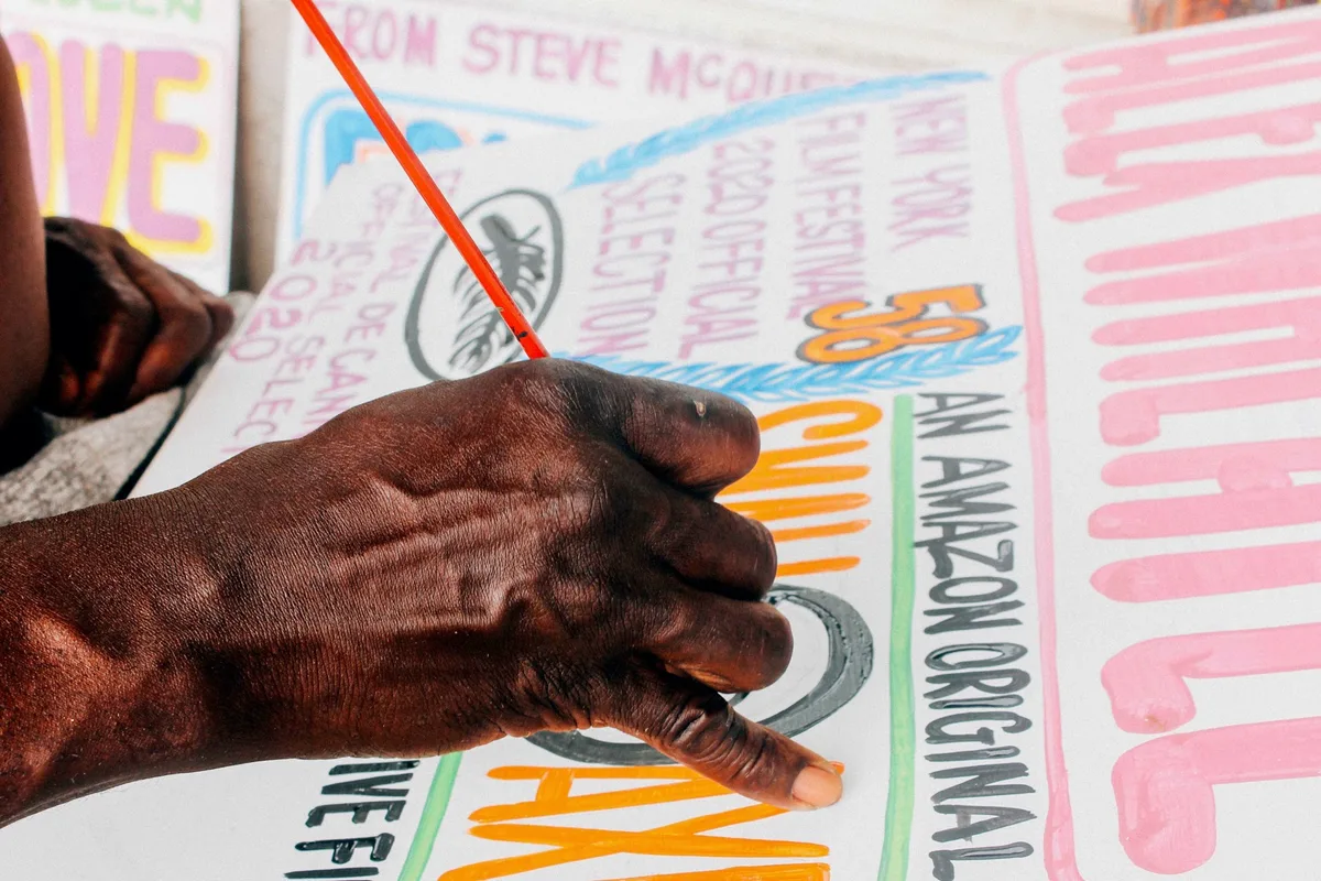 A hand holding a fine brush, painting red lines